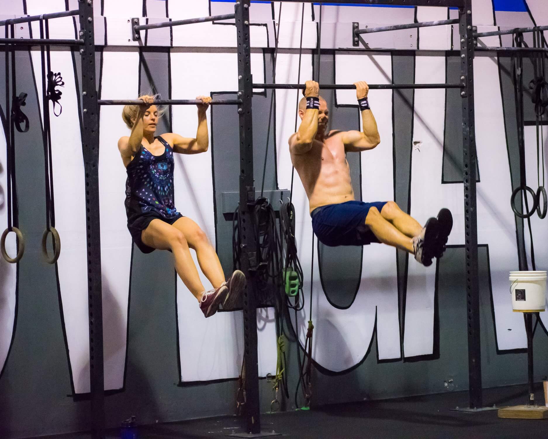 two people do pull ups at indoor gym