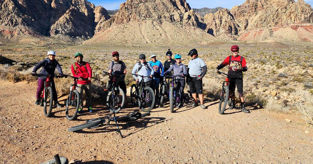 group of bicyclists stand in front of desert landscape