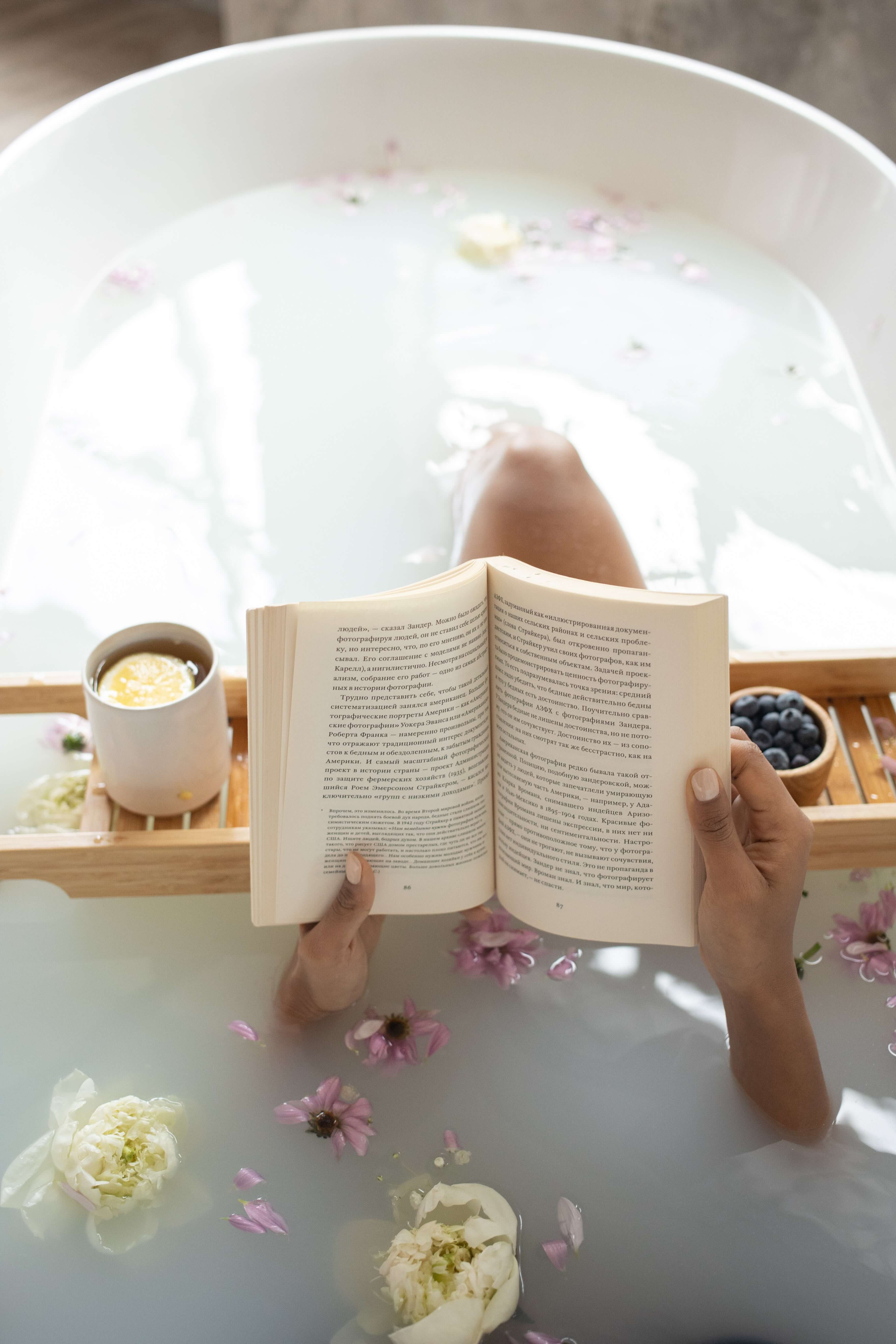 person reads book in bath with coffee tray 